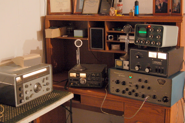 Mike Rome Wisconsin hamshack. Sitting in a corner on the right wall is a computer desk with a Kenwood TS-520, Phasemaster II B, and Ameritron AL-811 with three 572B tubes. On top of the linear is a Heathkit SB610 monitor scope. On top of the Kenwood is its D-104 mic. On top of the phasemaster is a power meter with the phasemaster's D-104.
