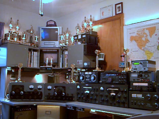 Ralph shows us a vintage AM station consisting of a Johnson Viking 500, Johnson Viking Valiant,  and a couple of Collins 75A4 receivers. Sitting on a couple shelves above are maybe a dozen old transmitting tubes in sockets with the filaments lit up giveing the room a nice glow.